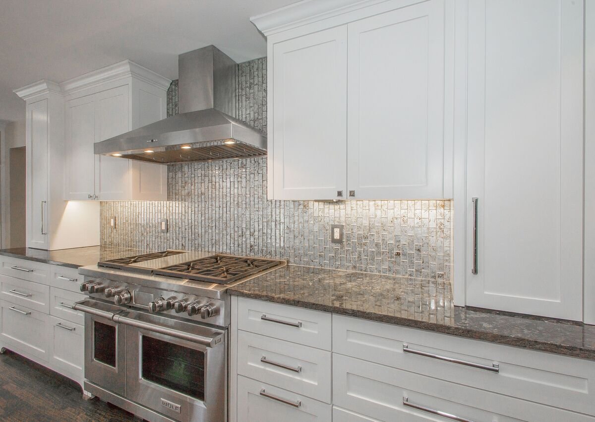 High-end kitchen remodel with mosaic backsplash behind oven and range hood and luxury countertop material