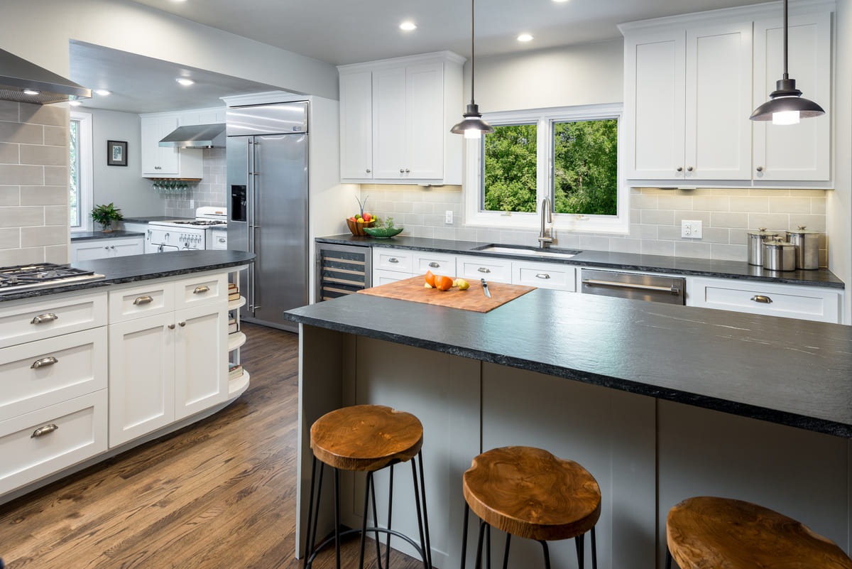 Two hanging light fixtures above kitchen island with three stools tucked in in Dallas kitchen remodel by Sardone | McLain